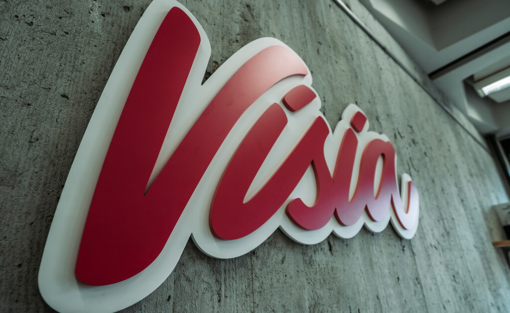Een rood-wit bord 'Vision', dat de recente rebranding van de huisstijl weerspiegelt, is gemonteerd op een betonnen muur in een kamer met ramen.