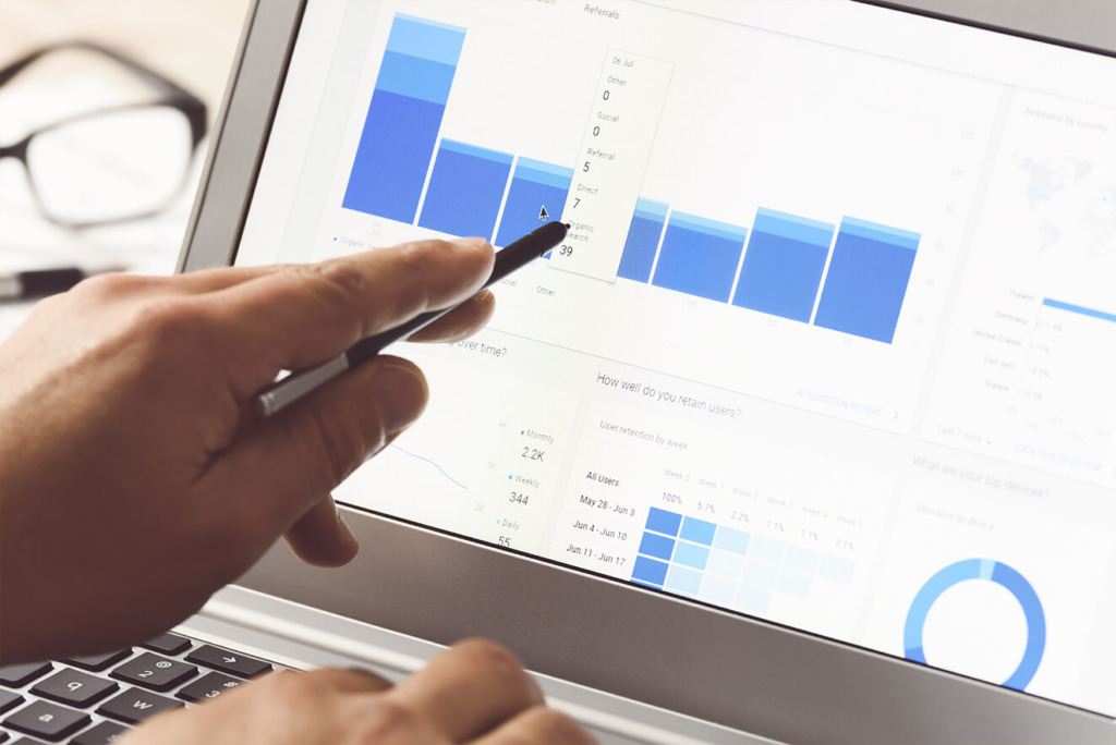 De hand van een persoon houdt een pen vast en wijst naar grafieken en diagrammen op een laptopscherm met analytische gegevens en zoekresultaten SERP-statistieken.
