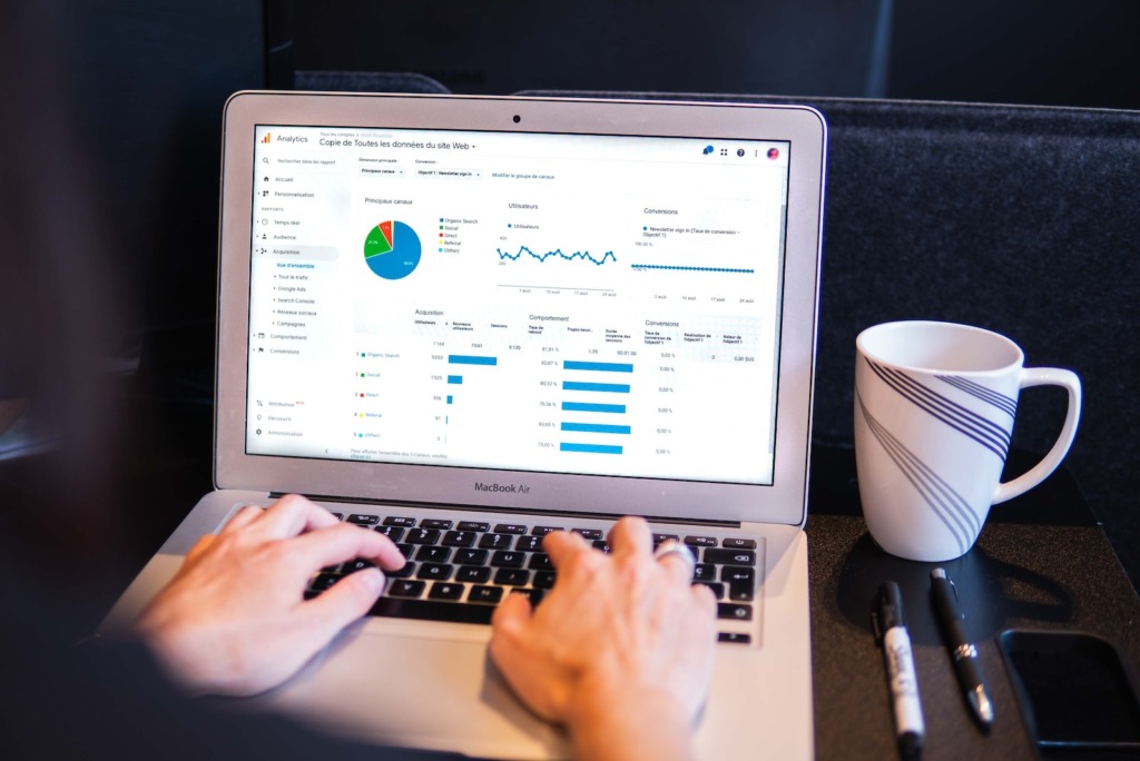 Persoon die gegevens analyseert op een laptop met grafieken en diagrammen, naast een wit koffiekopje en pennen op een tafel, gericht op het genereren van B2C-leads.