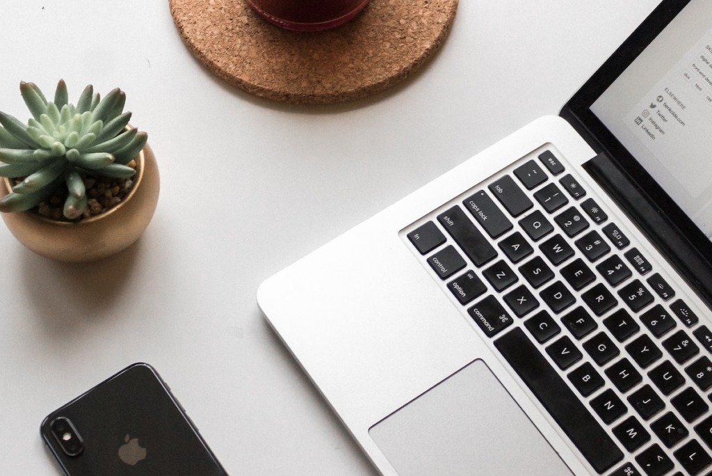 space gray iPhone X beside turned on laptop beside coffee and succulent plant