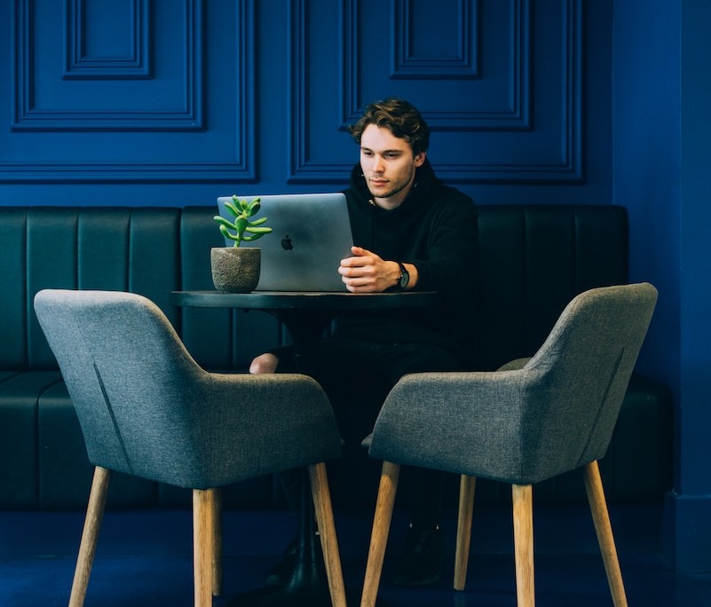 man sitting on couch with looking at his MacBook on table