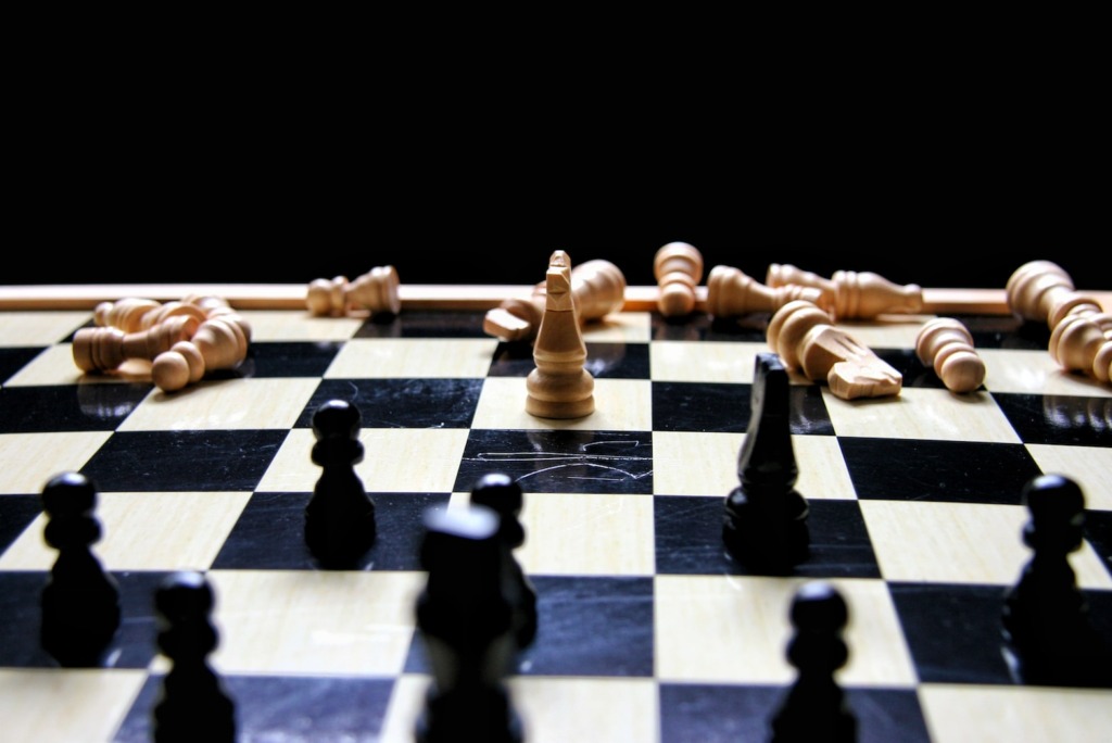 Een schaakbord met zwarte stukken in het spel en witte stukken die op de achtergrond bij weinig licht omvallen, onderscheidend van concurrentie door de dramatische weergave van de nasleep van een spel.