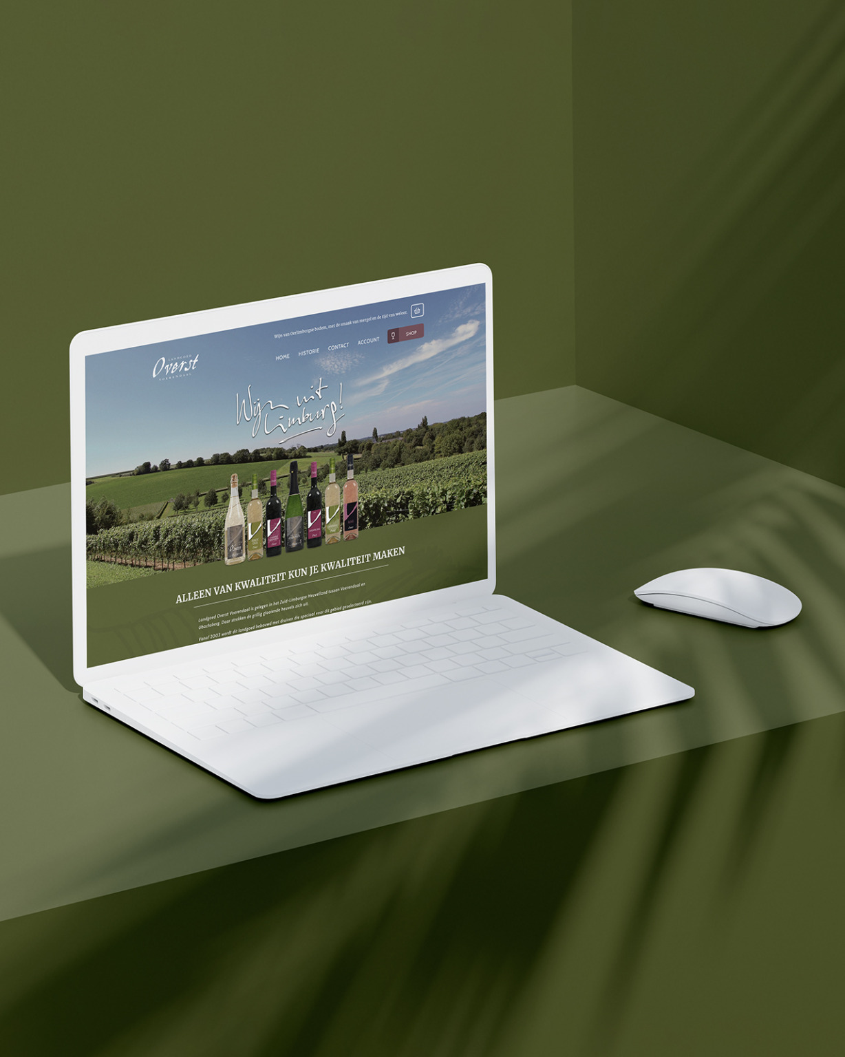 Open laptop en muis op een groen oppervlak met een Landgoed-website met flessen wijn en een wijngaardachtergrond.
