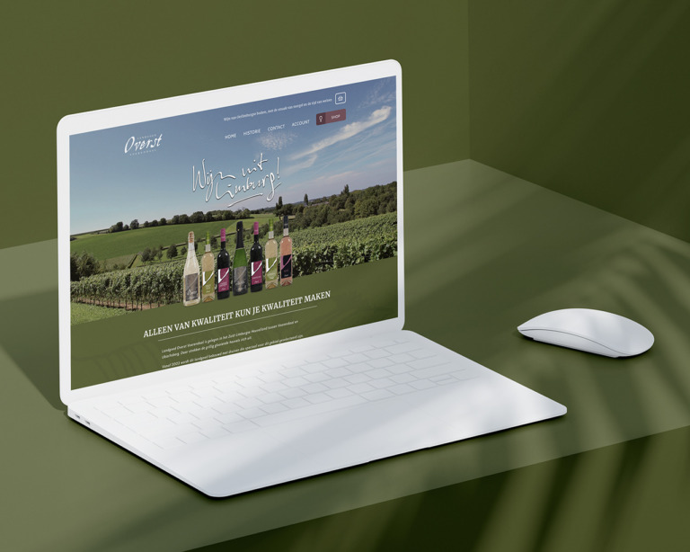 Open laptop en muis op een groen oppervlak met een Landgoed-website met flessen wijn en een wijngaardachtergrond.
