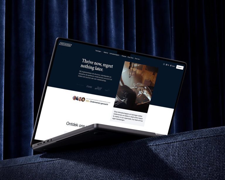 Op een donkerblauwe bank met een gordijn op de achtergrond staat een dunne laptop open; op het scherm is een website te zien — zijn doelgerichte uitstraling belichaamt de principes van Straight-Line Leadership.