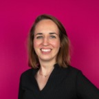 Een vrouw met schouderlang haar glimlacht tegen een felroze achtergrond en straalt zelfvertrouwen uit. Ze draagt een zwarte top en belichaamt de dynamische geest van Heuvel Marketing.