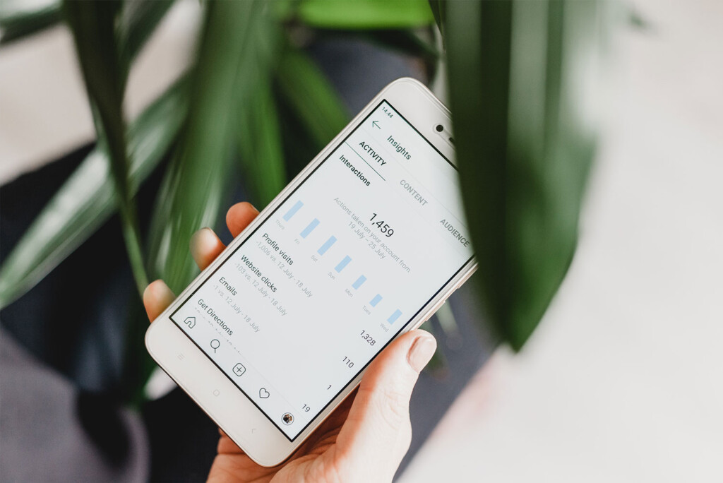 Hand die een smartphone vasthoudt die analyses en inzichten weergeeft tegen een achtergrond van groene bladeren, perfect voor degenen die de website uitbesteden willen beheren.