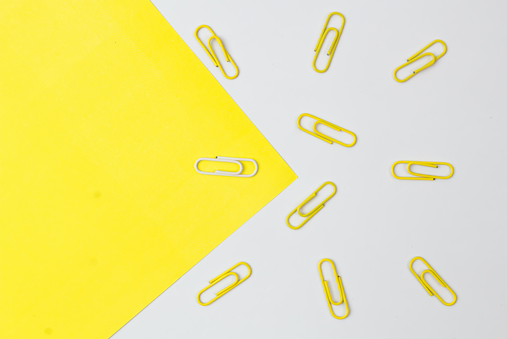 Gele paperclips, die op backlinks lijken, zijn in een cirkelvormig patroon rond een enkel geel vel papier op een witte achtergrond gerangschikt.