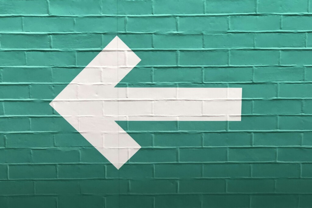 Witte pijl die naar links wijst op een groene bakstenen muurachtergrond, die de herpositioneringsmerkreis symboliseert.