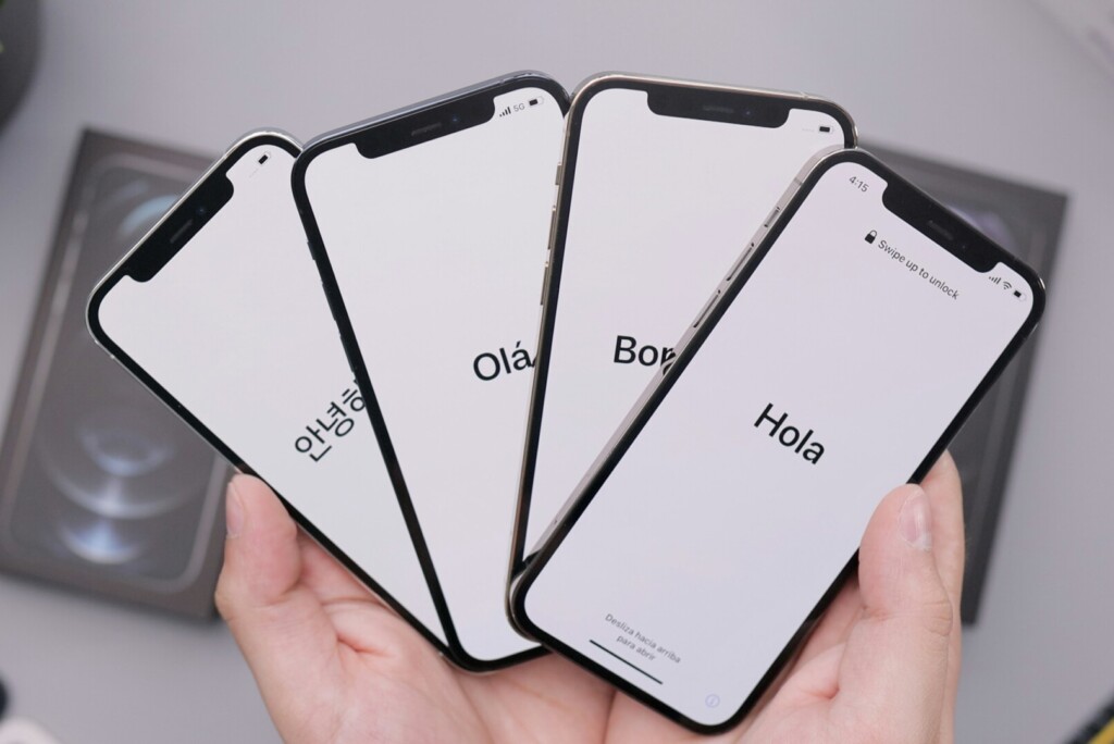 Een persoon houdt vier smartphones vast die begroetingen in verschillende talen op hun scherm weergeven, wat het belang aantoont van een mobielvriendelijke website voor het bereiken van een divers publiek.