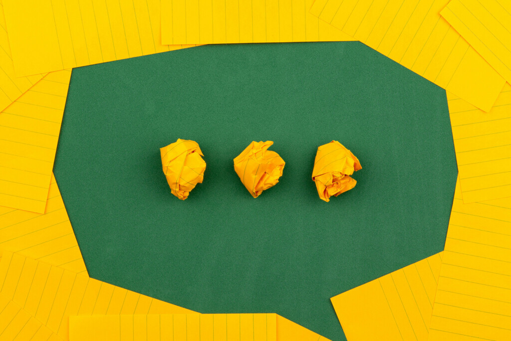 Geel verfrommeld papier in een groene tekstballonuitsnede, omringd door geel gelinieerde vellen papier - perfect voor als je een slogan probeert te bedenken.
