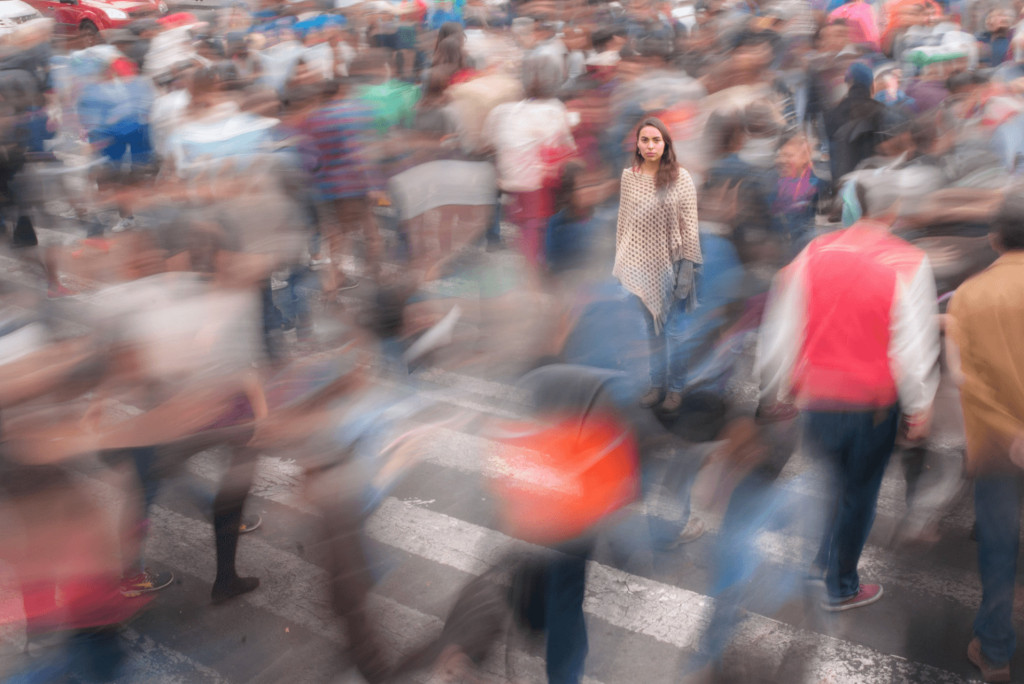 Een vrouw staat stil te midden van een drukke, wazige menigte die de straat oversteekt. Ze kijkt rustig recht voor zich uit, alsof ze met gemak bezoekerswebsites kan bezoeken.