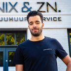 Een persoon staat buiten Tweewiel-Centrum, met een Hub Nix-bord op de achtergrond.