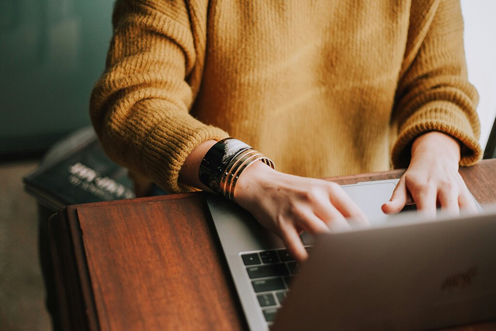 Een persoon in een gele trui typt op een laptop aan een houten bureau, gefocust op het toepassen van tips voor website-optimalisatie om de online prestaties te verbeteren.