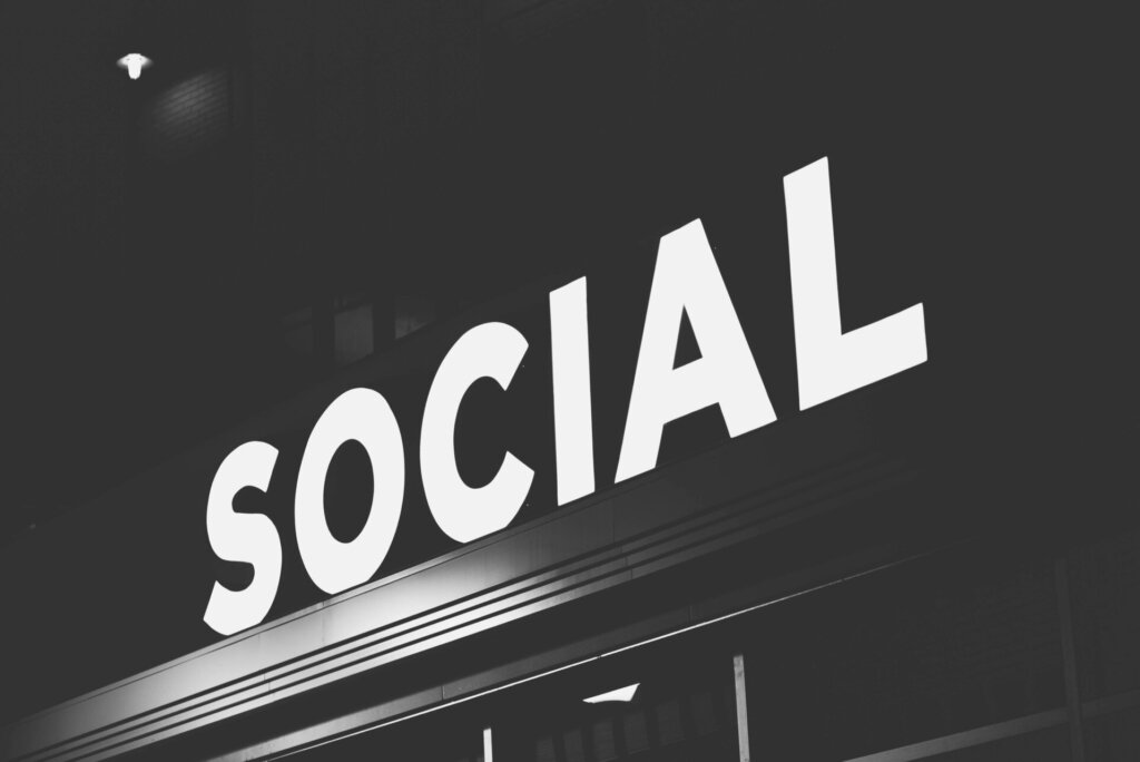 Monochroom beeld van een groot, verlicht 'SOCIAL'-bord tegen een donkere achtergrond, symbool voor de heldere verbindingen en netwerken die via sociale media ontstaan.