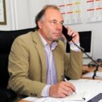 Een man in een bruine blazer telefoneert aan een bureau in Consuminderhuis Parkstad, terwijl hij met een pen in een notitieblok schrijft.