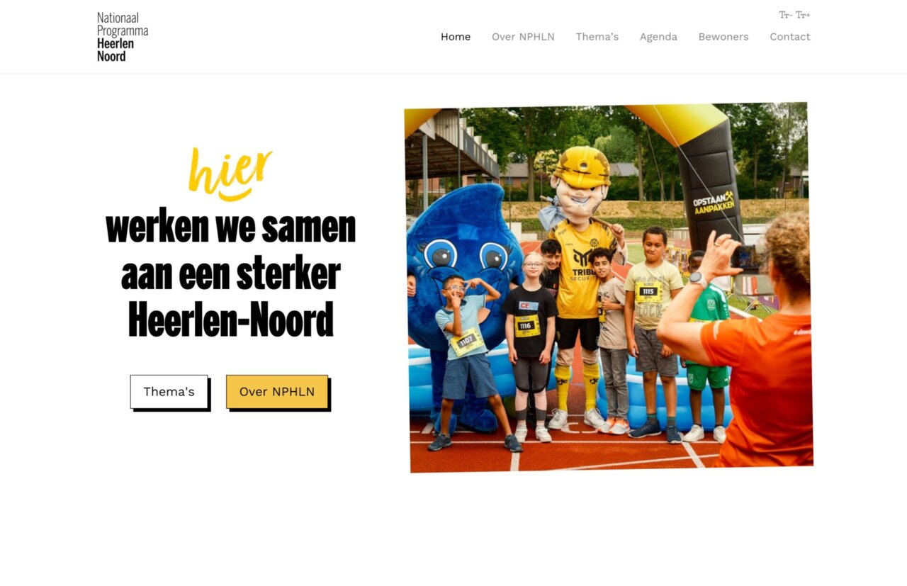 Een groep kinderen en volwassenen poseert buiten tijdens een sportevenement met een mascotte en fotograaf.