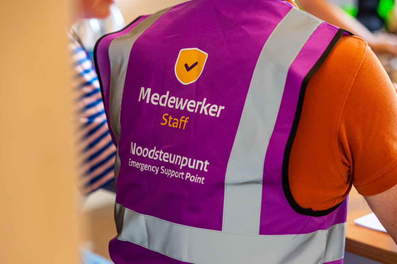 Iemand in een paars vest met de opschriften ‘Staff’ en ‘Emergency Support Point’ — onderdeel van het Pilot Noodsteunpunten-initiatief.